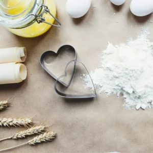 Ausstechformen: Zwischen Eiern, Weizenaehren, einem Glasbehälter und verstreutem Mehl liegen zwei Herz-Austechformen.