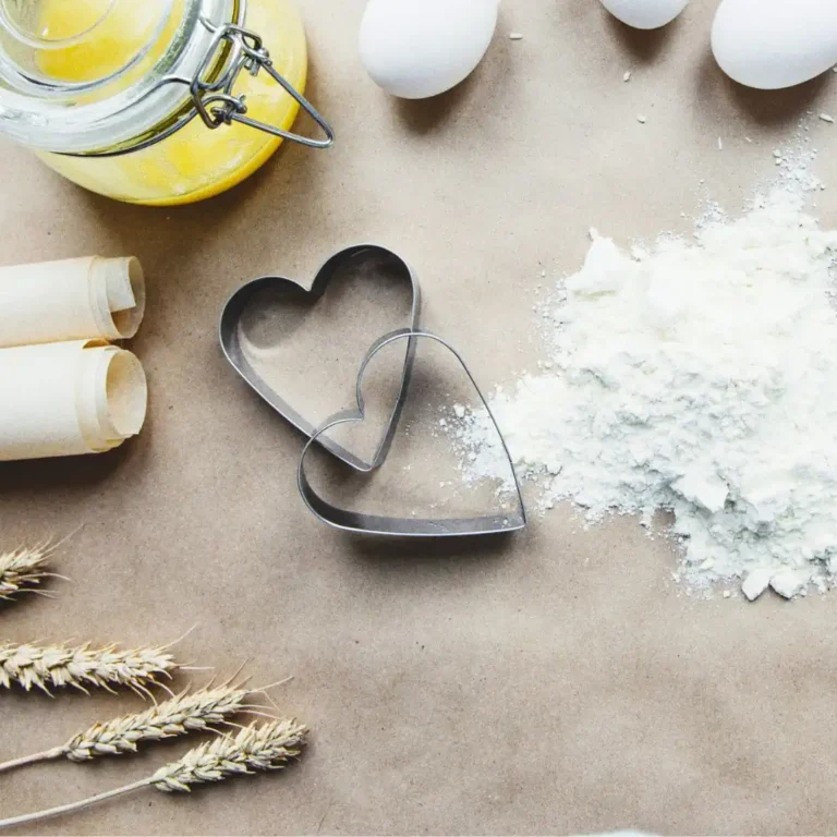 Ausstechformen: Zwischen Eiern, Weizenaehren, einem Glasbehälter und verstreutem Mehl liegen zwei Herz-Austechformen.